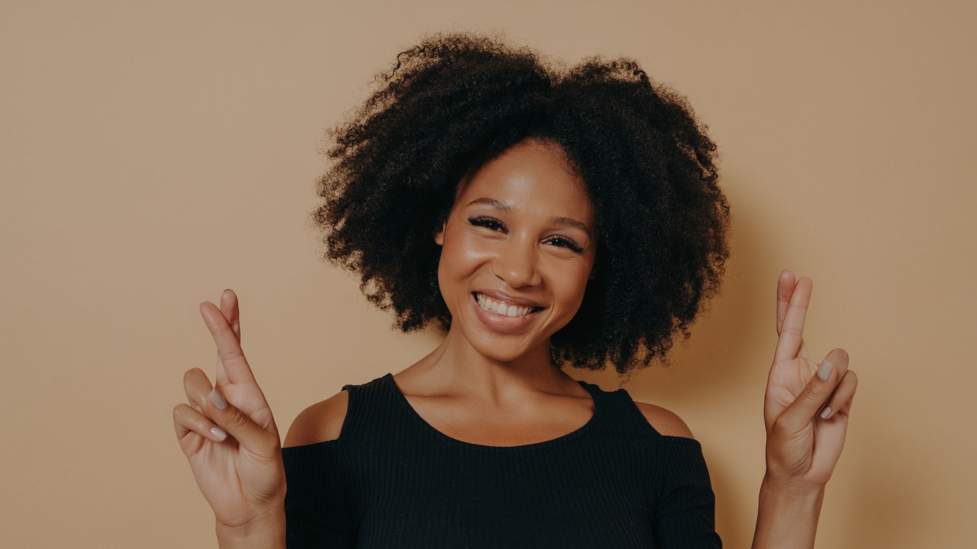 Portrait of happy young african woman standing isolated over dark beige background with copy space