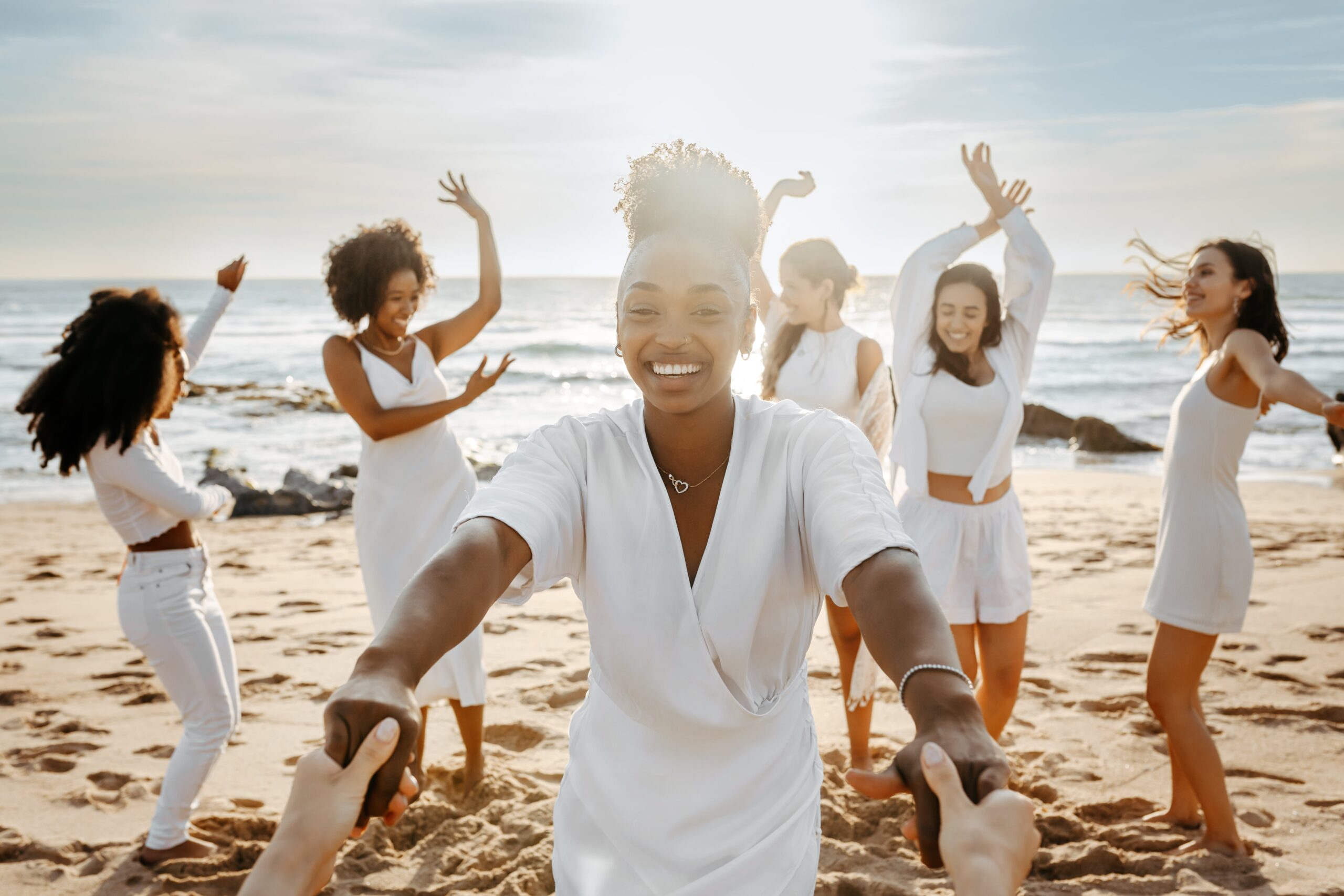 Diverse group of happy young female friends having fun outdoors on the beach, women celebrating